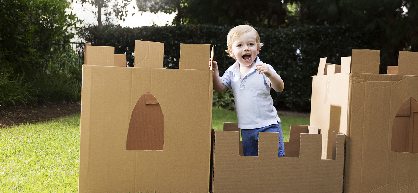 young boy plays in the yard with a castle made from cardboard box