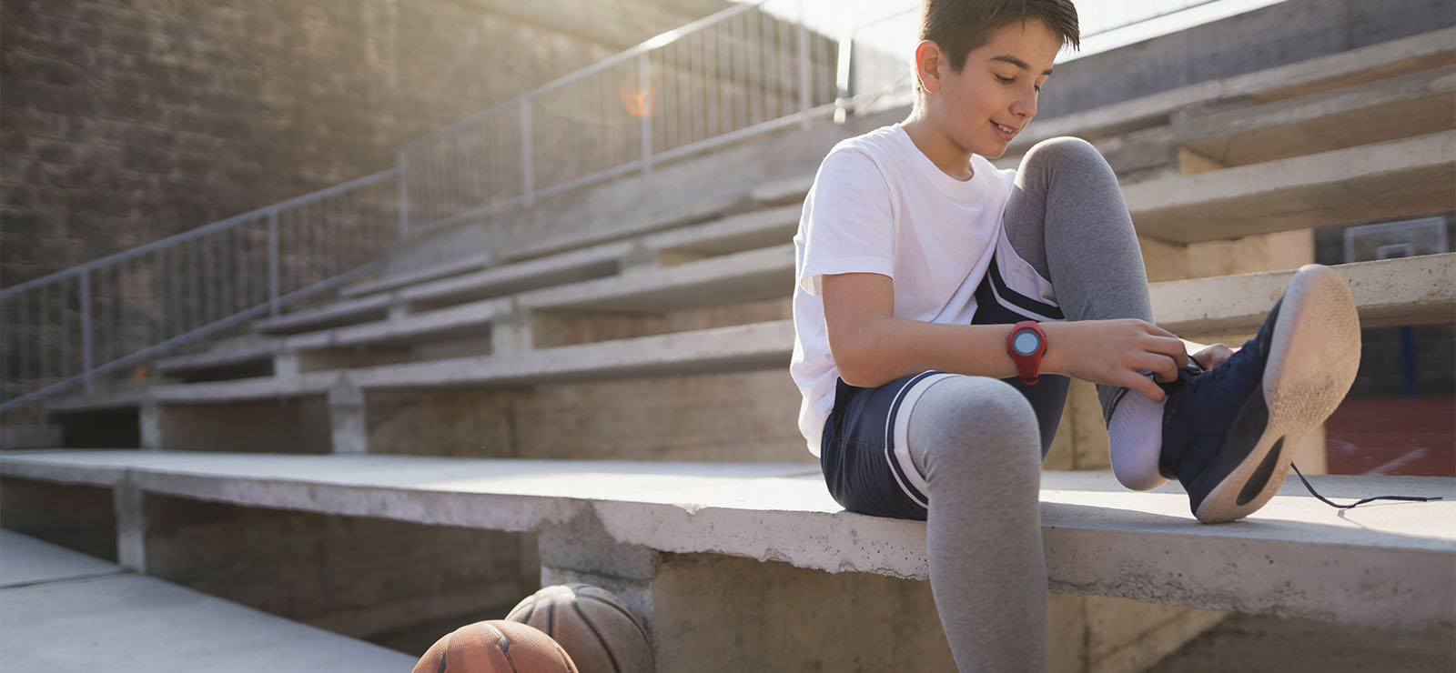 A teen tying his shoe, sitting on a stadium seat.