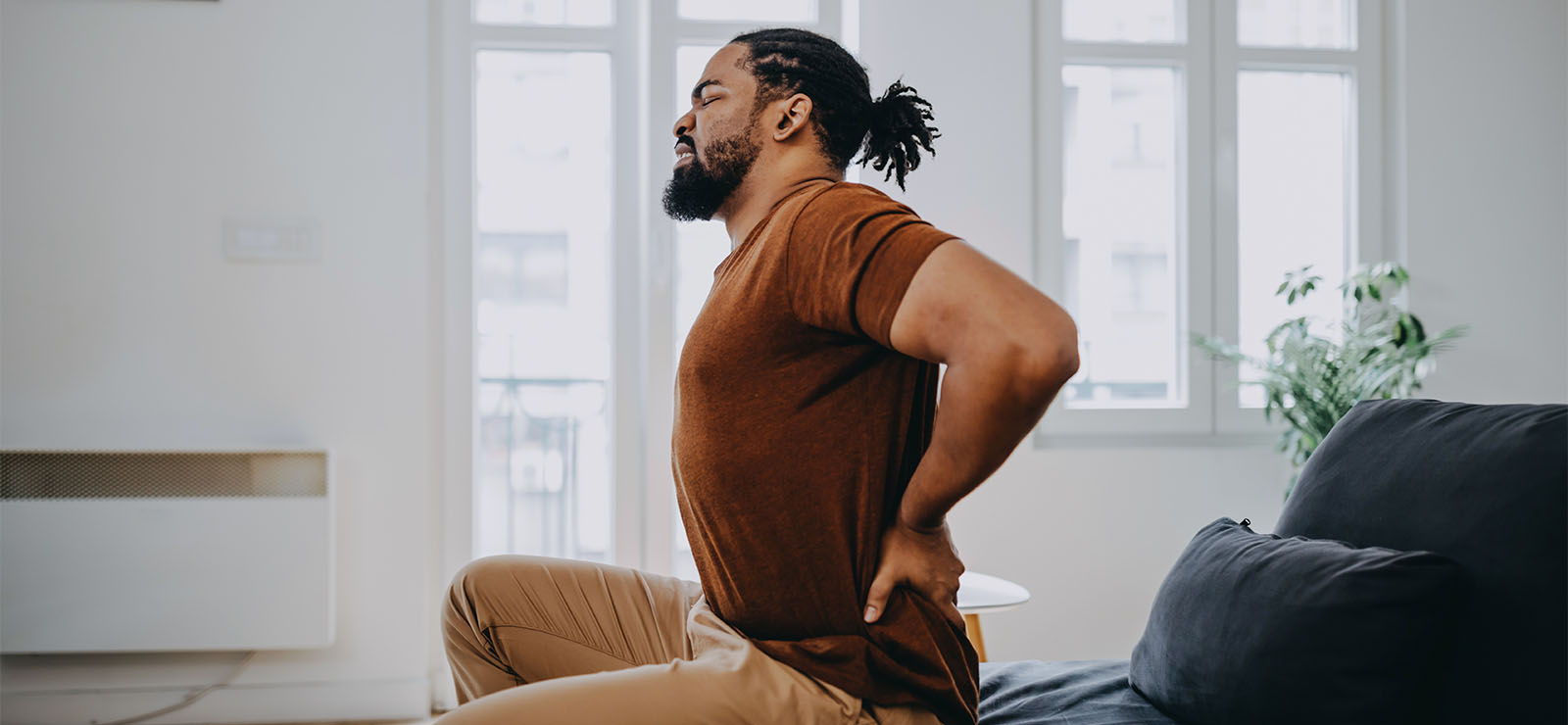 A man winces in pain as he touches his lower back.