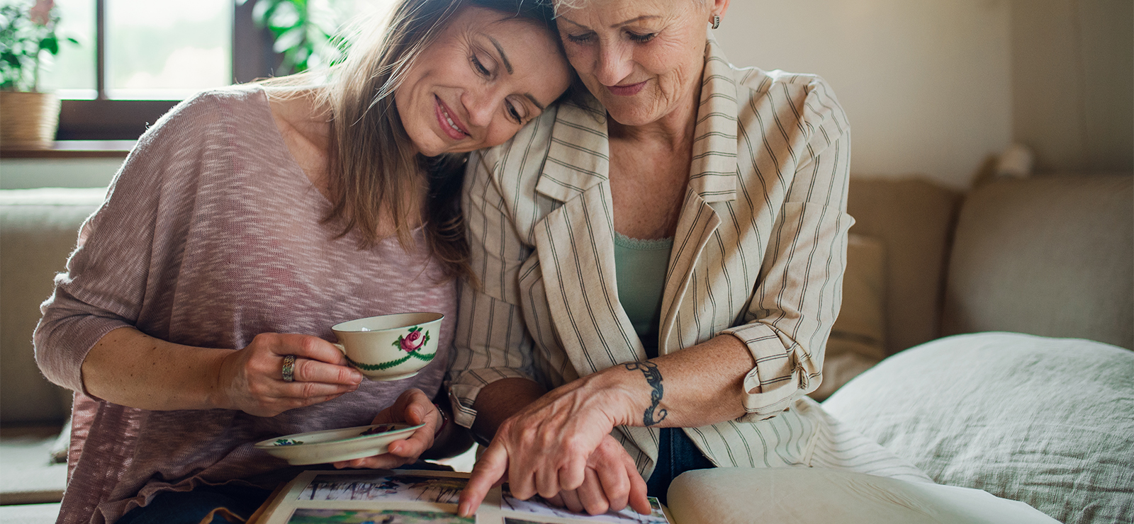 A mother and daughter sitting on a bed, smiling and hugging.