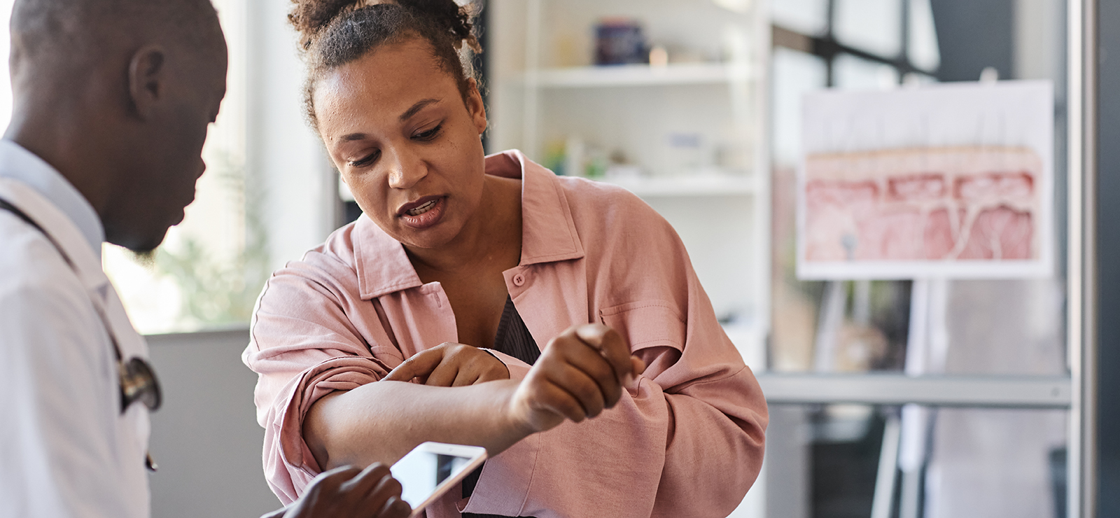 A photo of a doctor examining skin on a patient's arm.