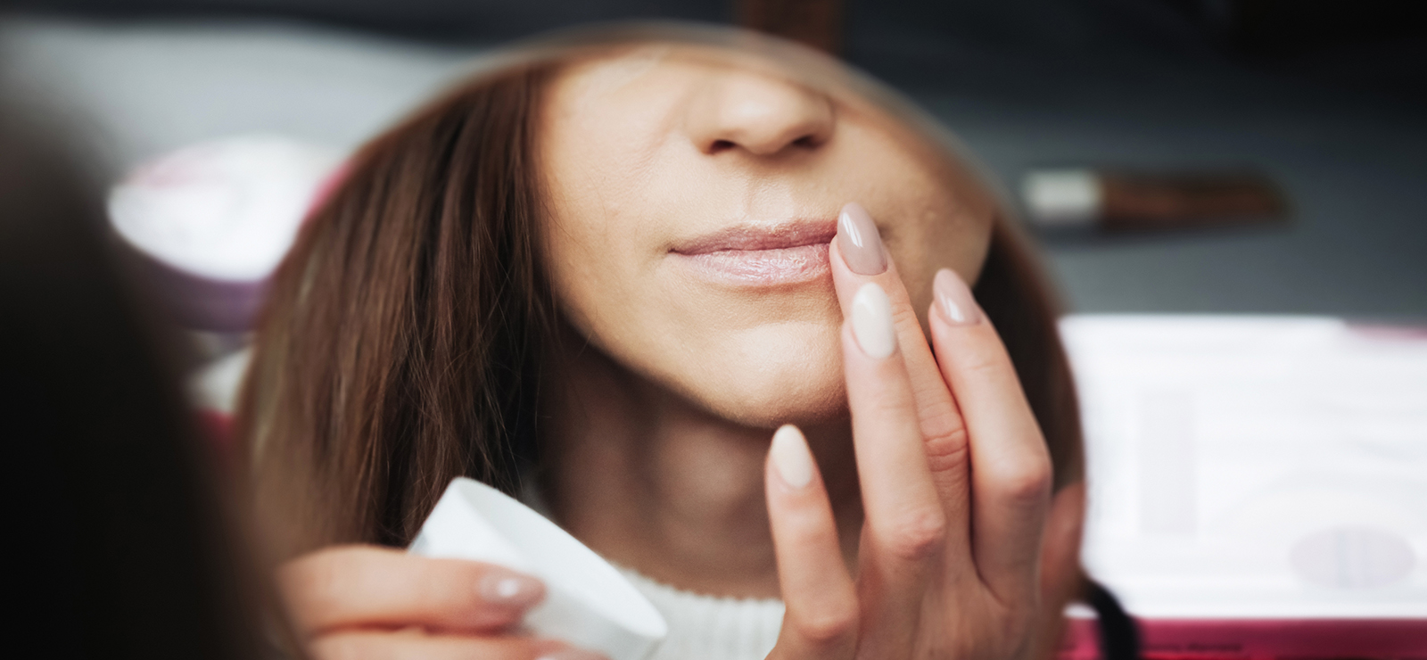 A woman putting on lip balm in a mirror.