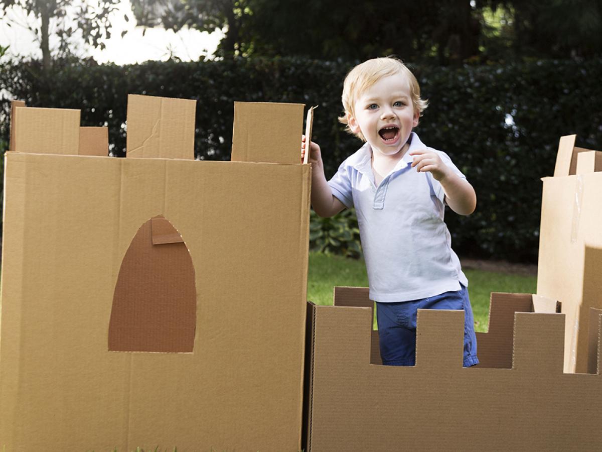 young boy plays in the yard with a castle made from cardboard box