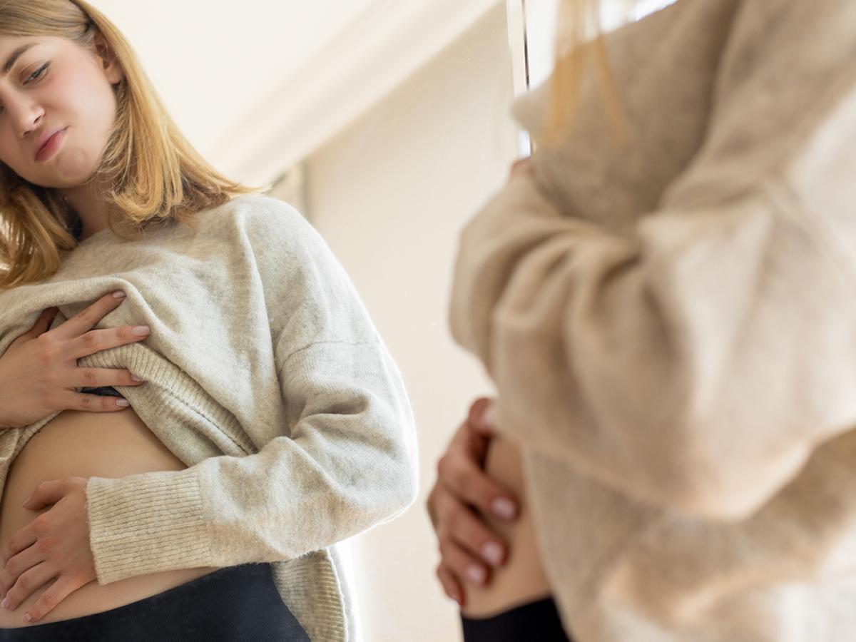 A woman looking at her stomach in the mirror.