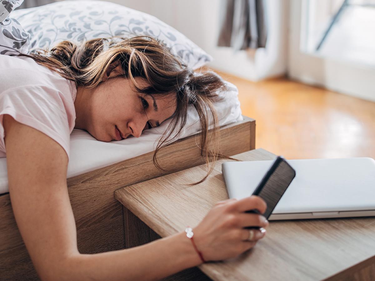 A woman lying in bed, looking at her phone.