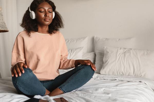 A woman meditating on the bed, listening to music.