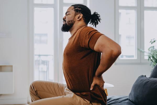 A man winces in pain as he touches his lower back.