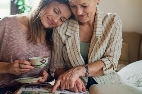 A mother and daughter sitting on a bed, smiling and hugging.