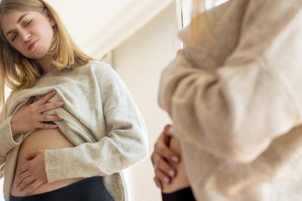 A woman looking at her stomach in the mirror.