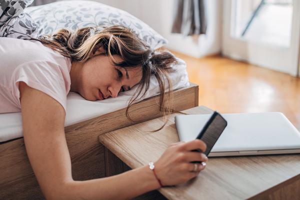 A woman lying in bed, looking at her phone.