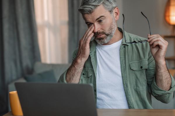 A man rubs his eyes after removing his glasses.