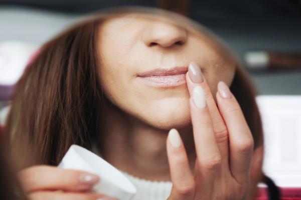 A woman putting on lip balm in a mirror.