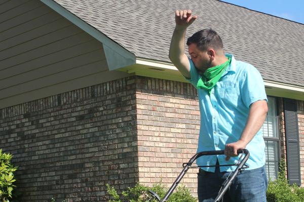 A man sneezing while mowing the lawn.