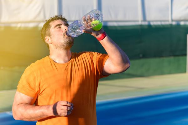 A man drinking a beverage after exercising outdoors.