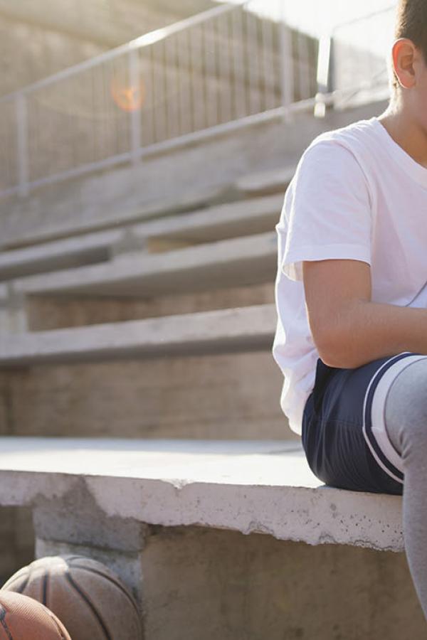 A teen tying his shoe, sitting on a stadium seat.