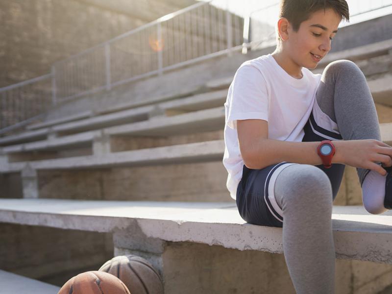 A teen tying his shoe, sitting on a stadium seat.