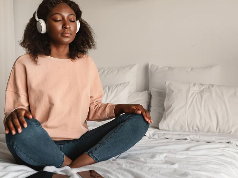 A woman meditating on the bed, listening to music.