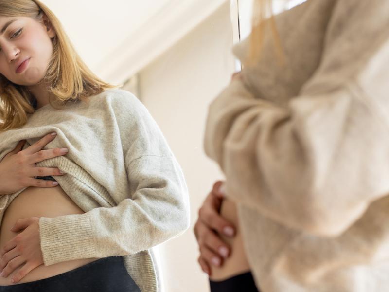A woman looking at her stomach in the mirror.