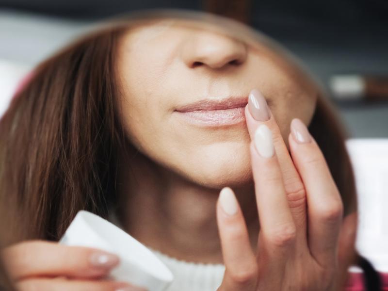 A woman putting on lip balm in a mirror.