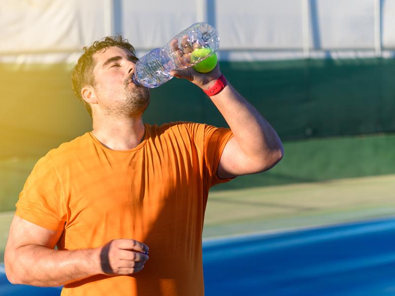 A man drinking a beverage after exercising outdoors.